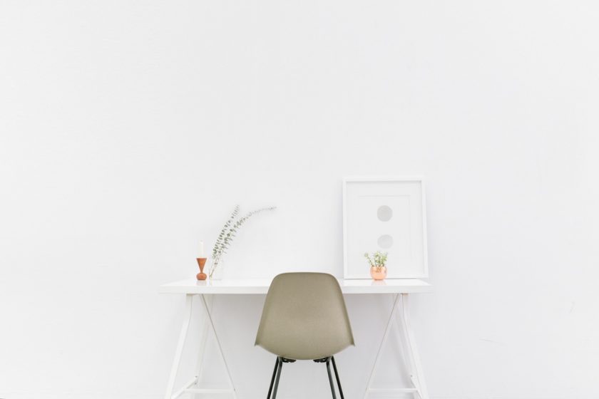 minimalist white desk with tan chair on plain white wall background