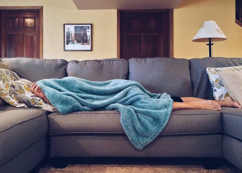 discouraged mom lying on the sofa covered by blue blanket in messy house