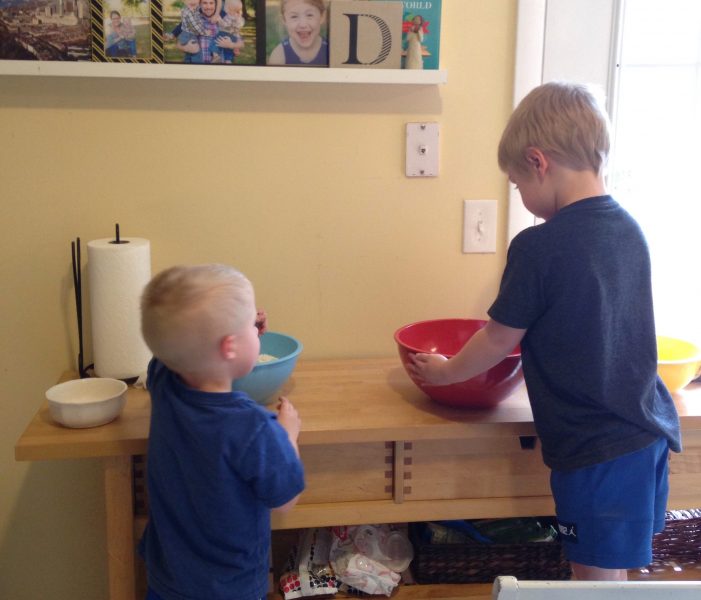 5-year-old and 3-year-old boys baking together at kitchen counter with mixing bowls