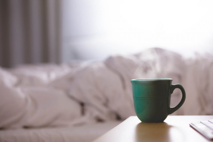 mom buried in covers refusing to wake up early, with coffee mug on nightstand