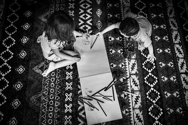 black and white, top down photo if a brother and sister drawing on large sketchpad with colored pencils