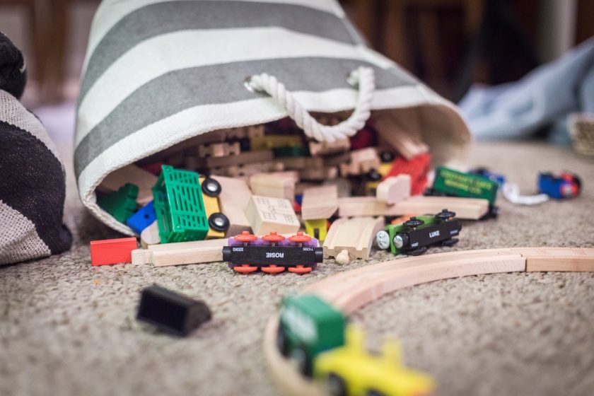 gray and white striped basket with toy trains and tracks spilled onto floor