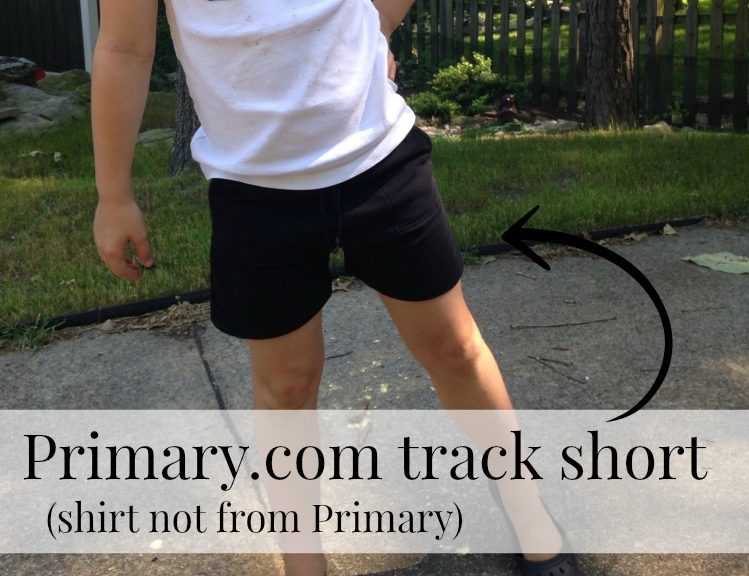 girl pictured from neck down, wearing white t-shirt and black Primary.com track shorts