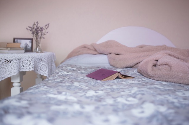 made bed with paisley duvet cover, with open, upside down purple book, and throw blanket