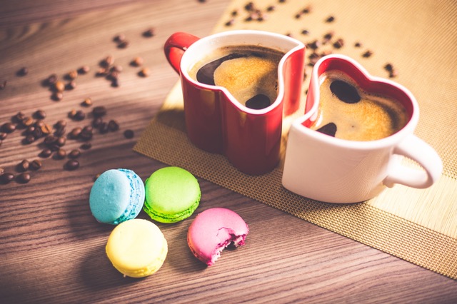two heart shaped mugs with colorful macaroons and coffee beans on kitchen table