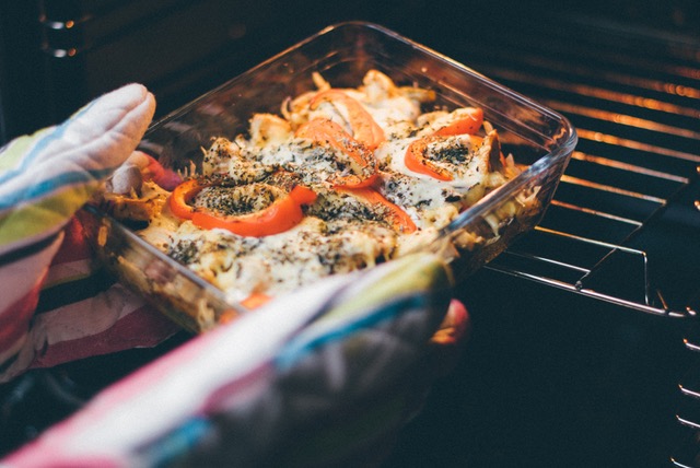 oven mitts holding pyrex casserole dish and putting into oven