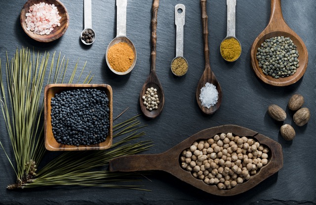 flat lay photo with metal and wooden spoons holding various spices on gray background