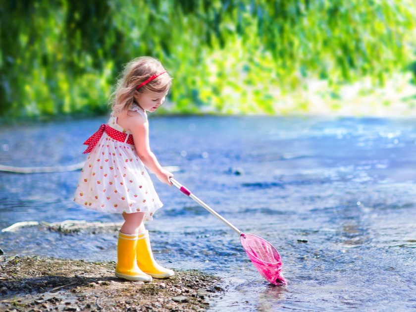 preschool age little girl in white dress and yellow rain boots playing outside in a lake as part of a homeschool day