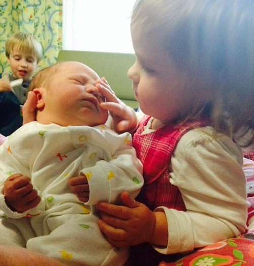 toddler holding new baby, touching face gently