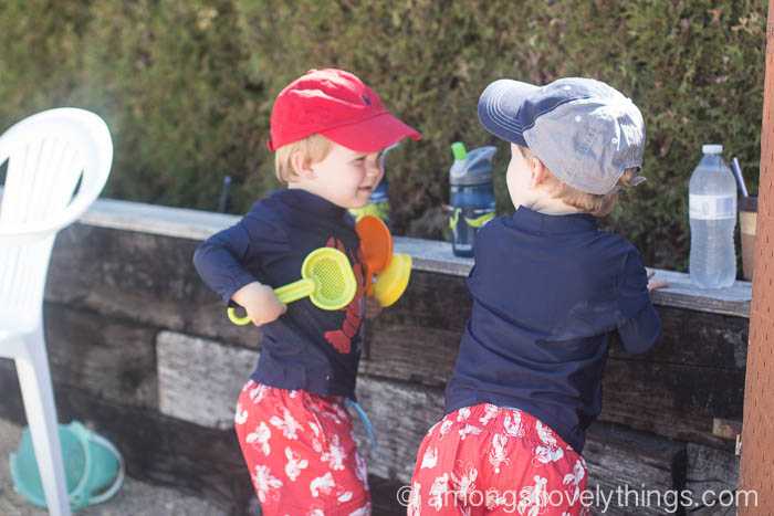 twins playing together with bathing suits and sand toys