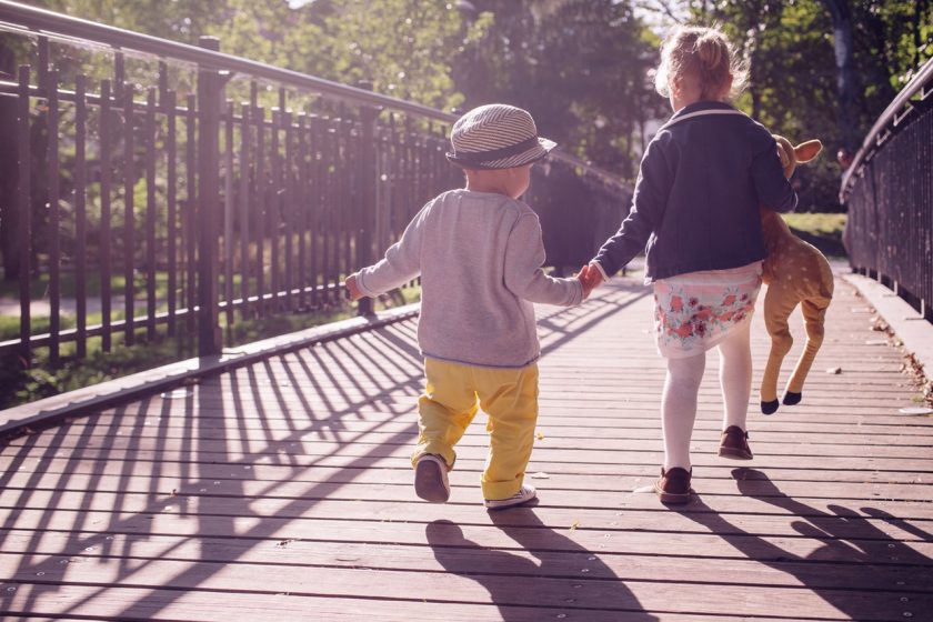 small children seen from behind, holding hands walking over bridge; one child holding stuffed animal