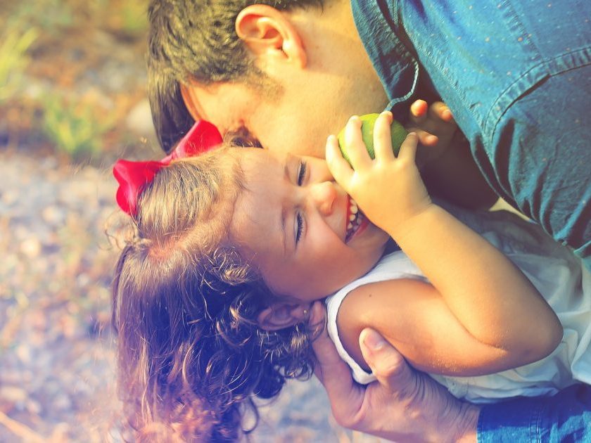 father hugging smiling young daughter with red bow in hair