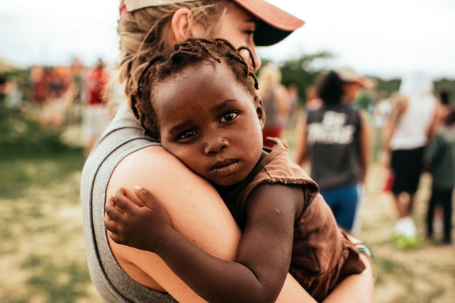 young white overseas worker - a young woman - holding black African young child in her arms