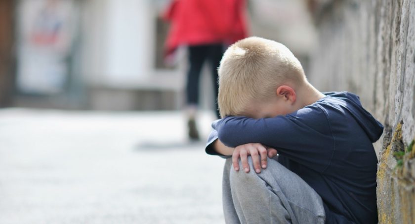 young boy with knees drawn up to chest, head in his arms crying