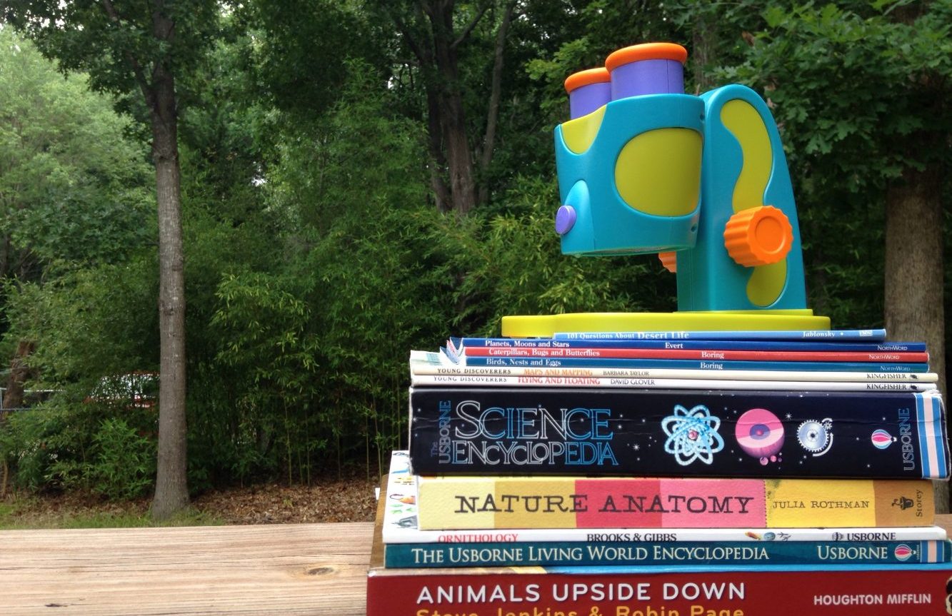 stack of science books for unschooling science sitting on a table, with a toy microscope on top.