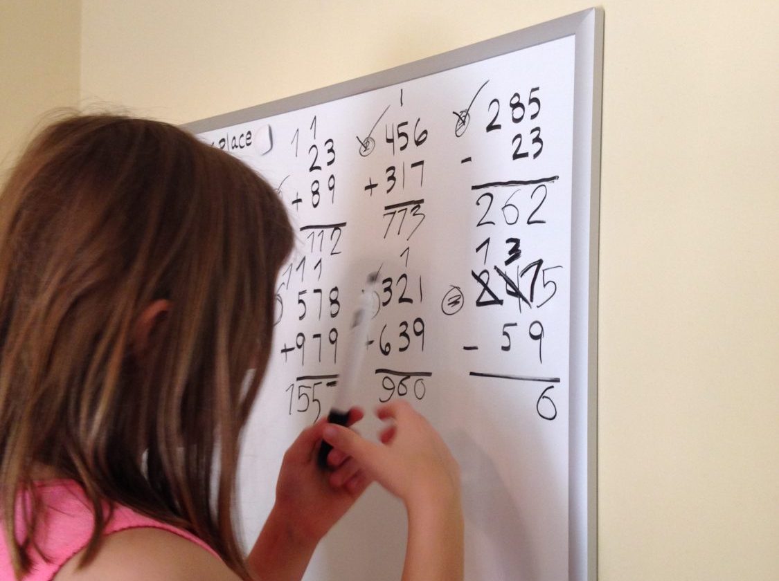 homeschooled child doing addition and subtraction problems on a white board