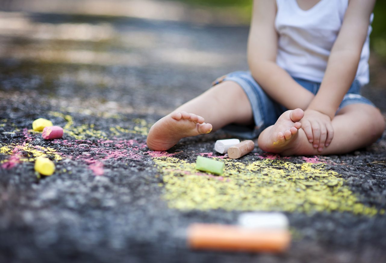 young child playing with chalk on pavement