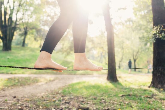 woman balancing barefoot on tightrope with trees and green park in background