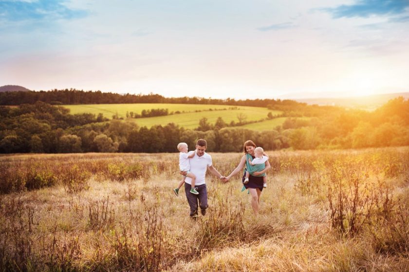 relaxed homeschooling parents walking in open field with two small children