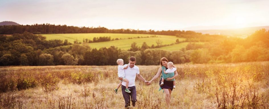 relaxed homeschooling parents walking in open field with two small children