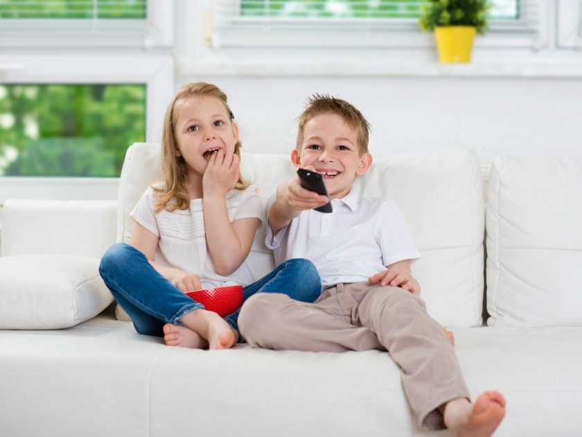 elementary brother and sister watching t.v. together on white couch