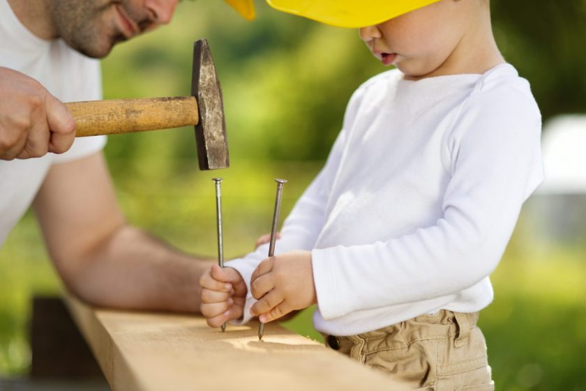 father teaching son woodworking, hammering nails into wooden plank