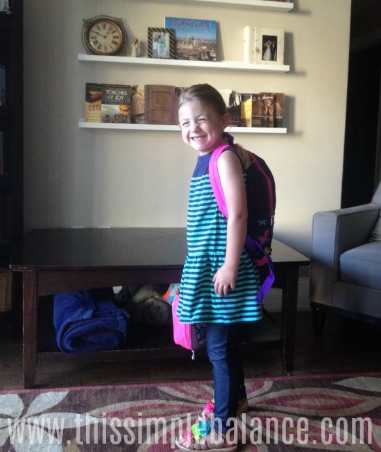 smiling 5-year-old girl dressed with backpack and lunch bag for first day of kindergarten at university model school