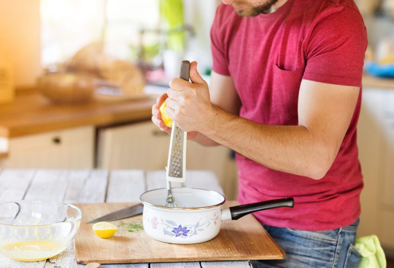 man grating lemon zest into pot sitting on cutting board in paperless kitchen