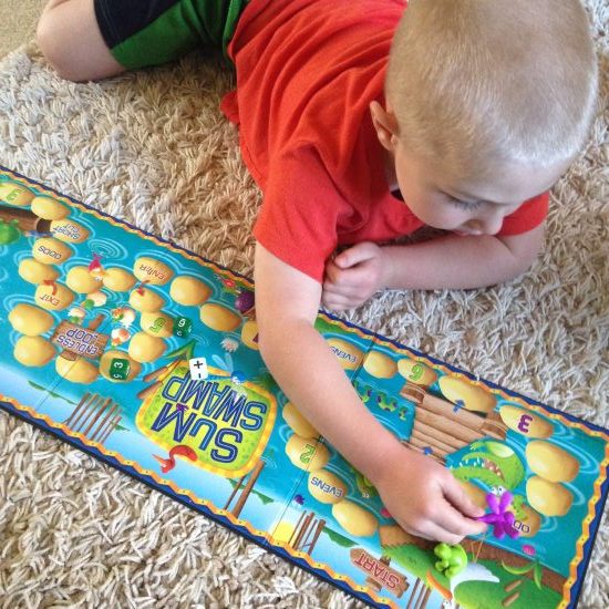 young boy playing Sum Swamp math board game on carpet