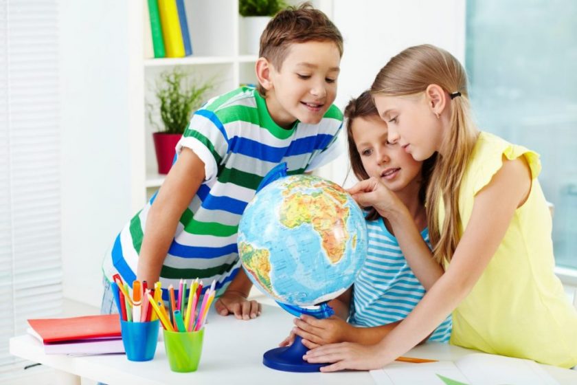 three older elementary aged children gathered around globe with cups of pencils on desk