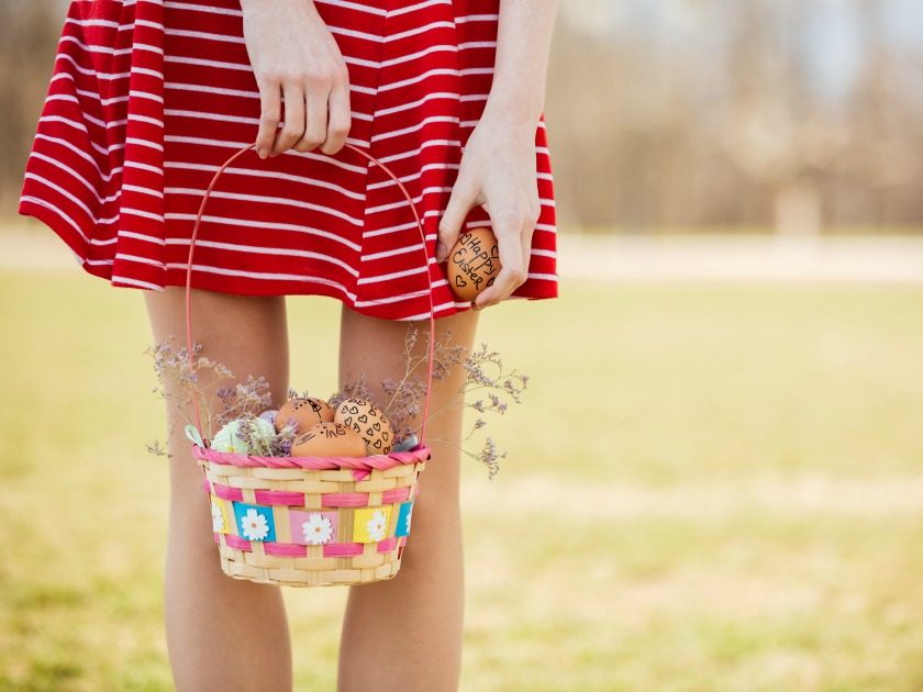 girl in red and white dress holding easter basket and egg with field in background