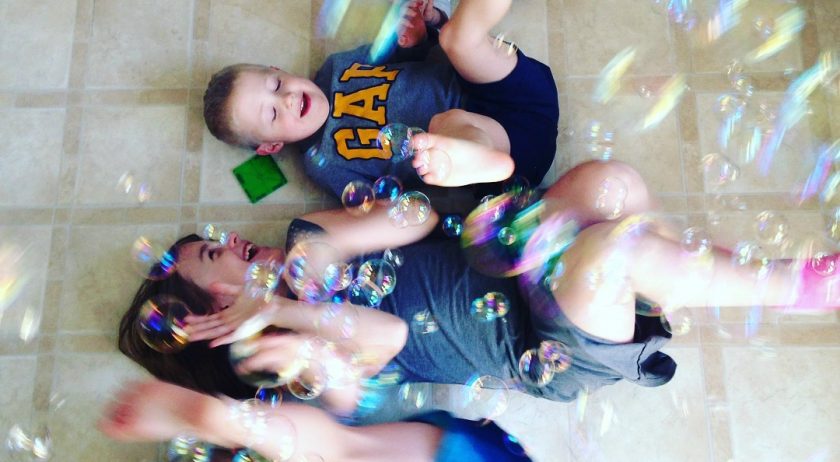 two siblings laughing while laying on kitchen floor, bubbles floating down on them