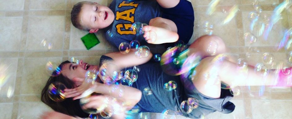 two siblings laughing while laying on kitchen floor, bubbles floating down on them