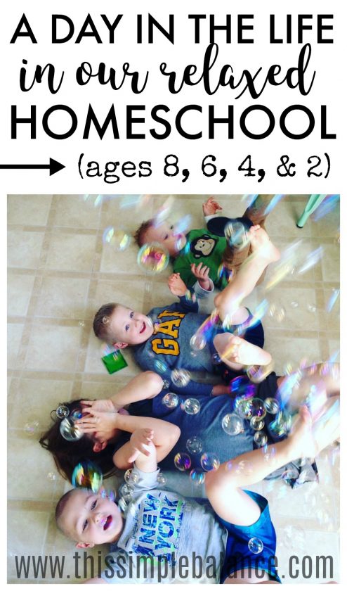 four siblings laying on kitchen floor with bubbles falling on them, laughing, with text overlay, "A day in the life in our relaxed homeschool (ages 8, 6, 4, & 2)"