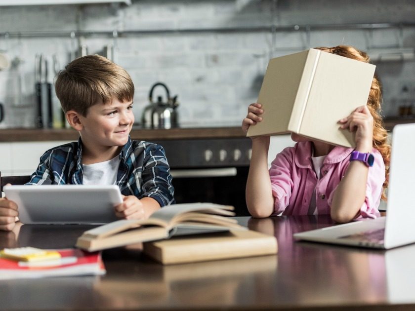 homeschooled brother and sister sitting at kitchen table reading books