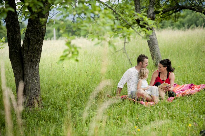 mom and dad sitting together outside with child reading a book