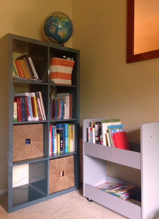 Homeschool living room with organized bookshelves, one for books that are owned, one rolling cart for library books