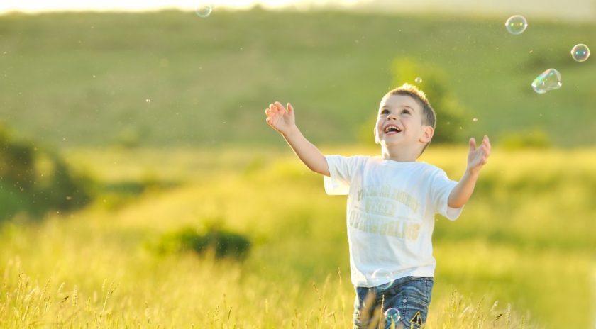 two-year-old boy running in field chasing bubbles