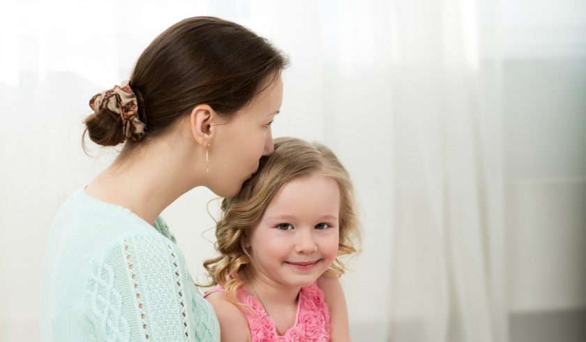 mom holding little girl on lap, kissing the top of her head