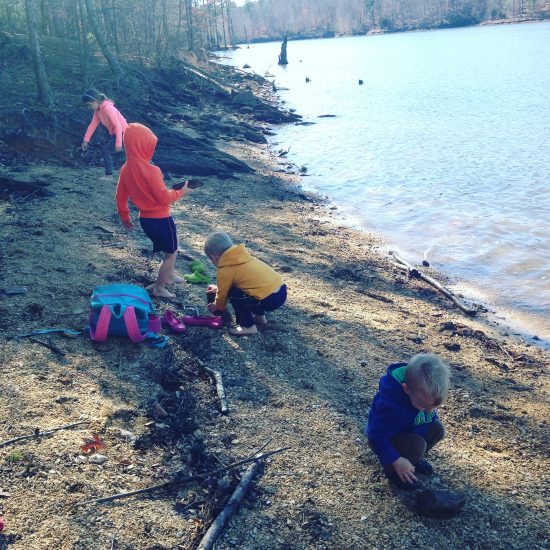 four young kids playing on the beach near a lake while on a nature walk