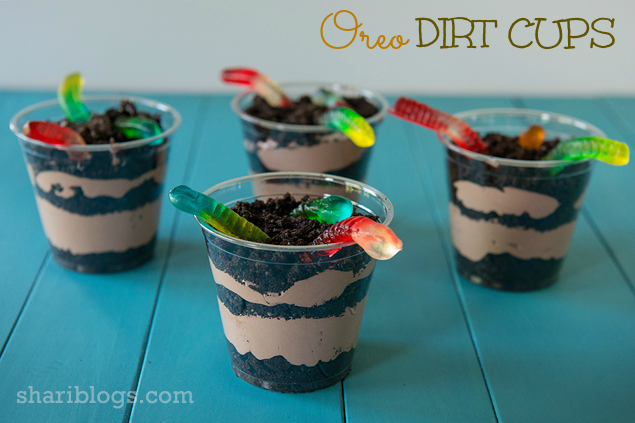 four Oreo Dirt Cups in clear plastic cups with pudding, crushed oreo and gummy worms on top