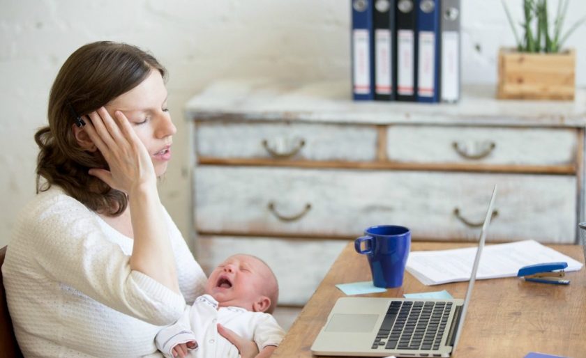 stressed stay at home mom trying to work with screaming newborn in her arms