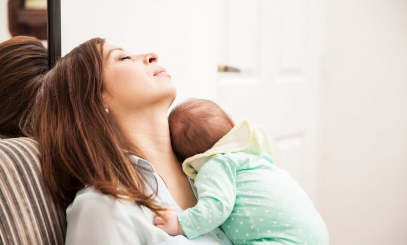 tired mom with eyes closed holding newborn while sitting in chair