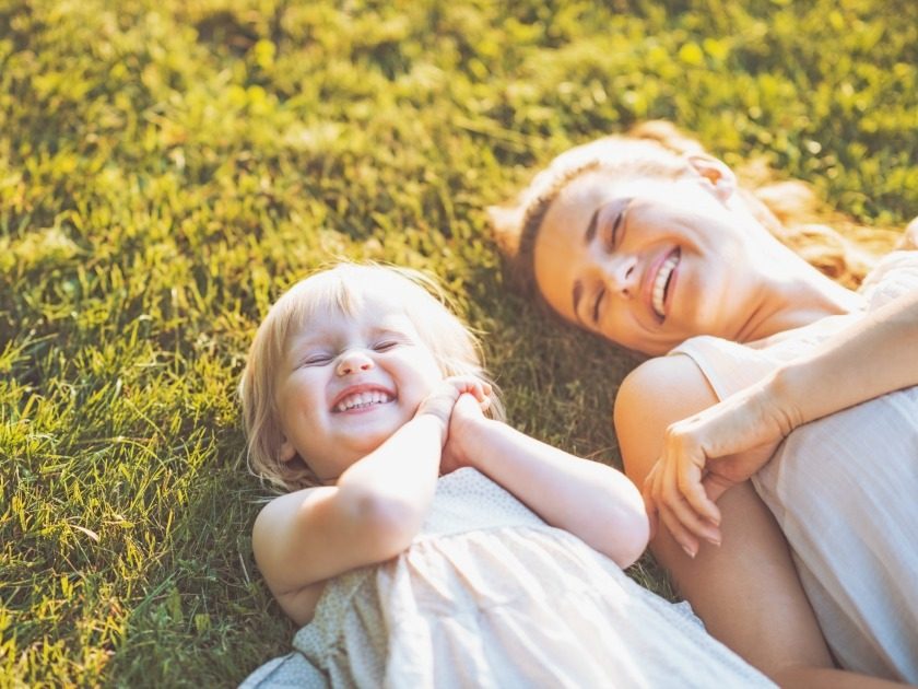 mom and toddler daughter lying on backs in a sunny field smiling