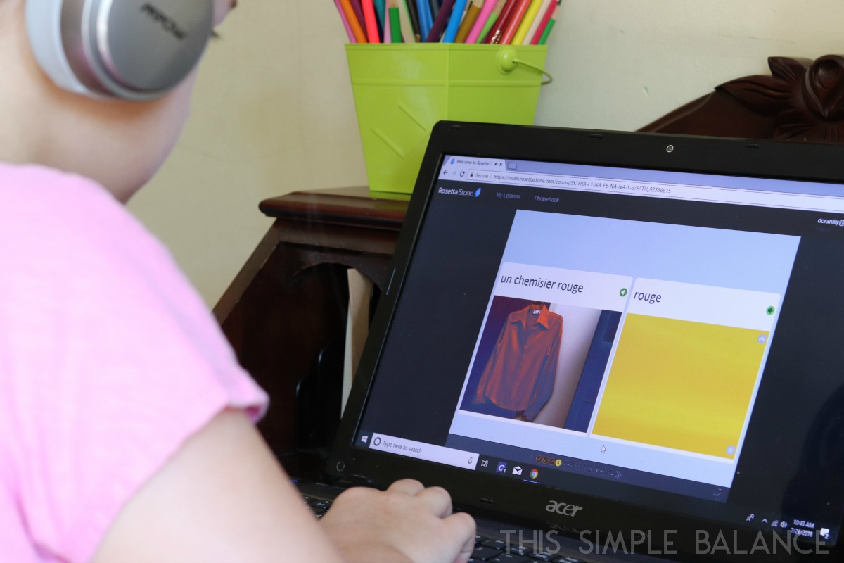 young girl looking at computer with Rosetta Stone french language instruction on screen, photograph of shirt with text above: "un chemisier rouge" 