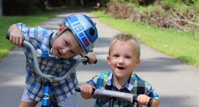 two homeschooled brothers riding bikes on path, staring straight at the camera with silly grins