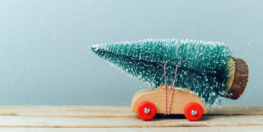 miniature toy wooden car with red wheels and christmas tree strapped to the roof