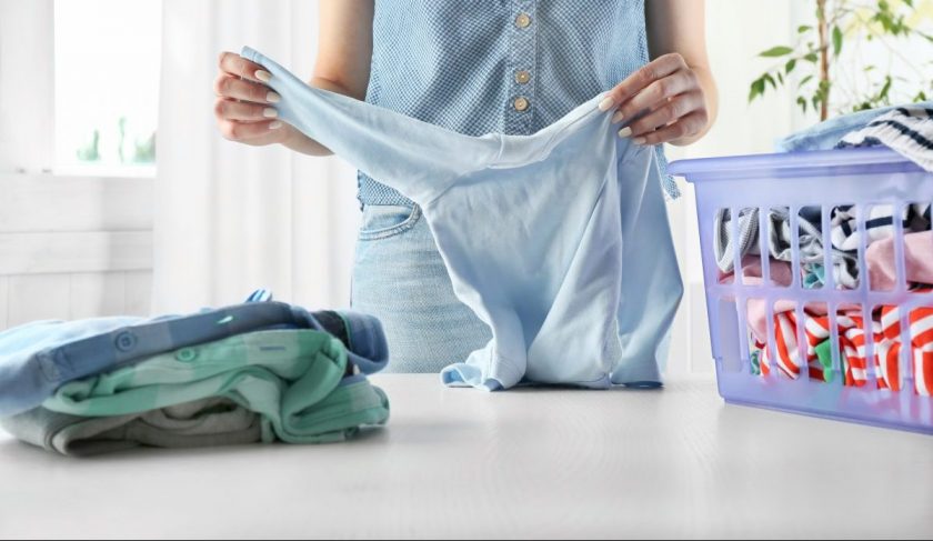 mom holding clean onesie, with laundry basket, contemplating not folding laundry