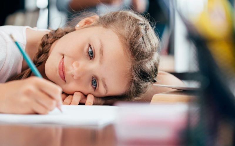 homeschooled girl working on brave writer arrow assignment, head on desk writing happily