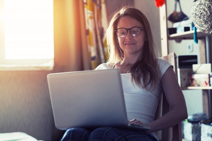 woman with glasses typing on laptop computer while sitting in armchair